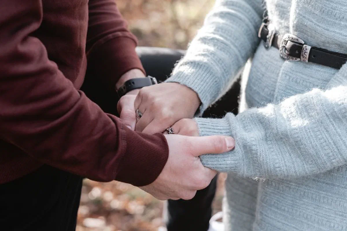 Close-up of a couple holding hands, showcasing affection and warmth in an autumn setting.