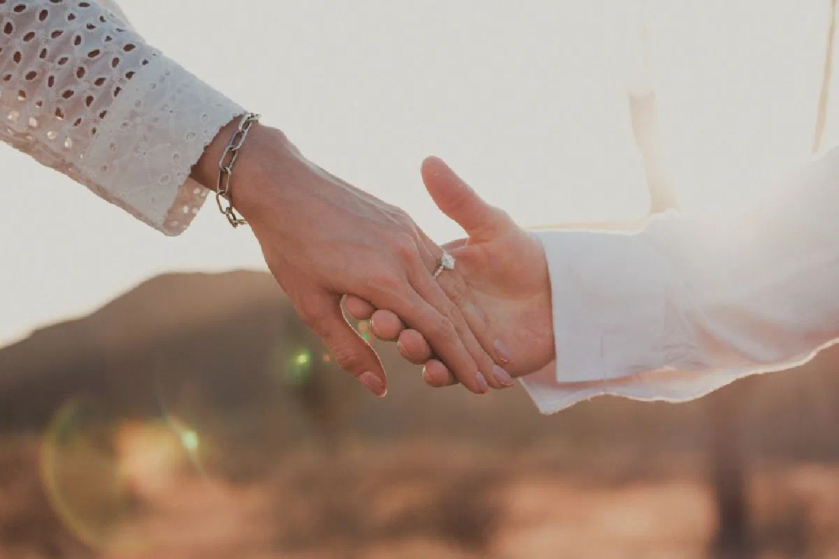 Close-up of a couple holding hands with an engagement ring at sunset, symbolizing love and commitment.