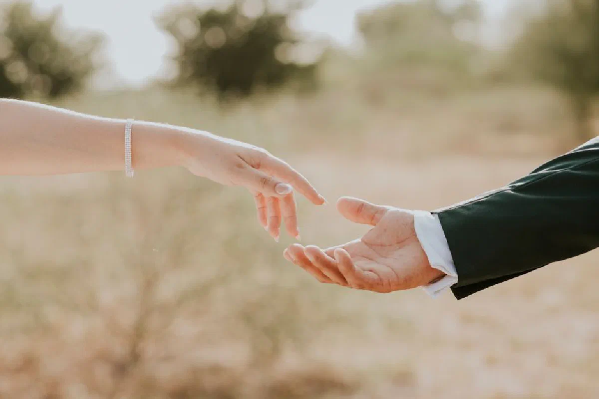 A touching moment captured outdoors with hands reaching towards each other, evoking a sense of connection.