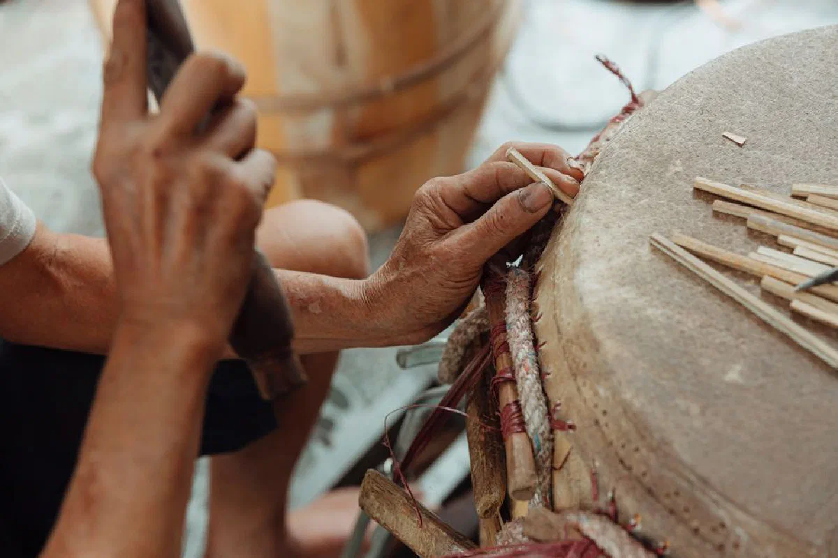 Close-up of hands crafting a traditional drum with sticks and tools.