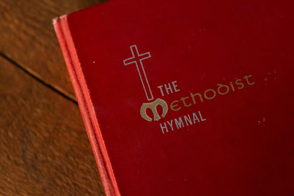 A red Methodist hymnal book with a cross symbol on a wooden table.