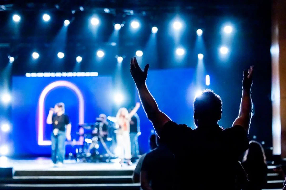 Silhouetted audience member raising hands during a live concert performance with vibrant stage lights.