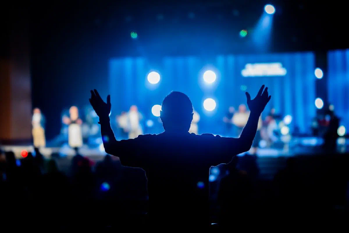 Silhouette of a person with raised hands at a vibrant concert stage.