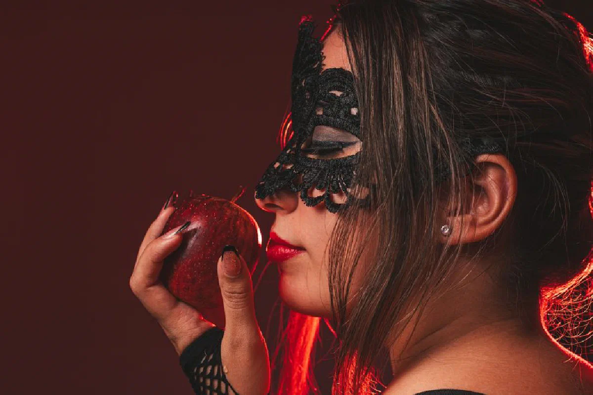 Elegant woman in lace mask holding an apple. Dark, moody portrait with a touch of mystery.