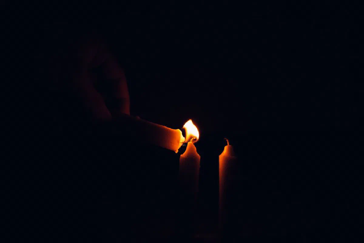 Moody candlelight scene showing a hand lighting candles with a dark background.