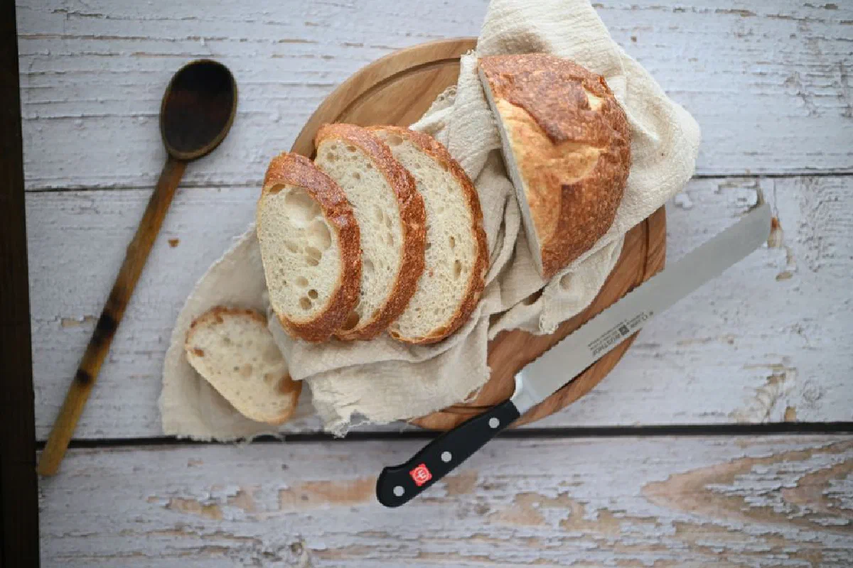 A top view of sliced bread loaf on a wooden tray with a knife and spoon nearby.