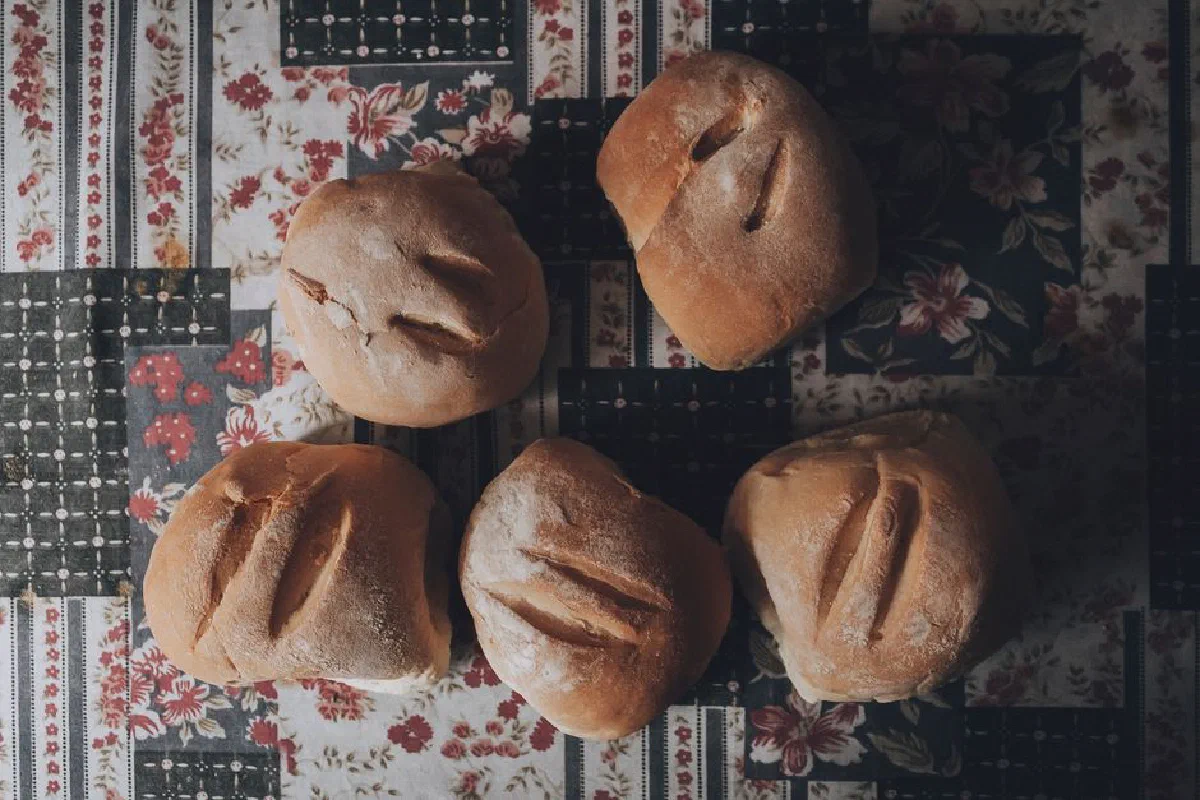 Top view of homemade bread rolls on a floral tablecloth, captured in ambient lighting.