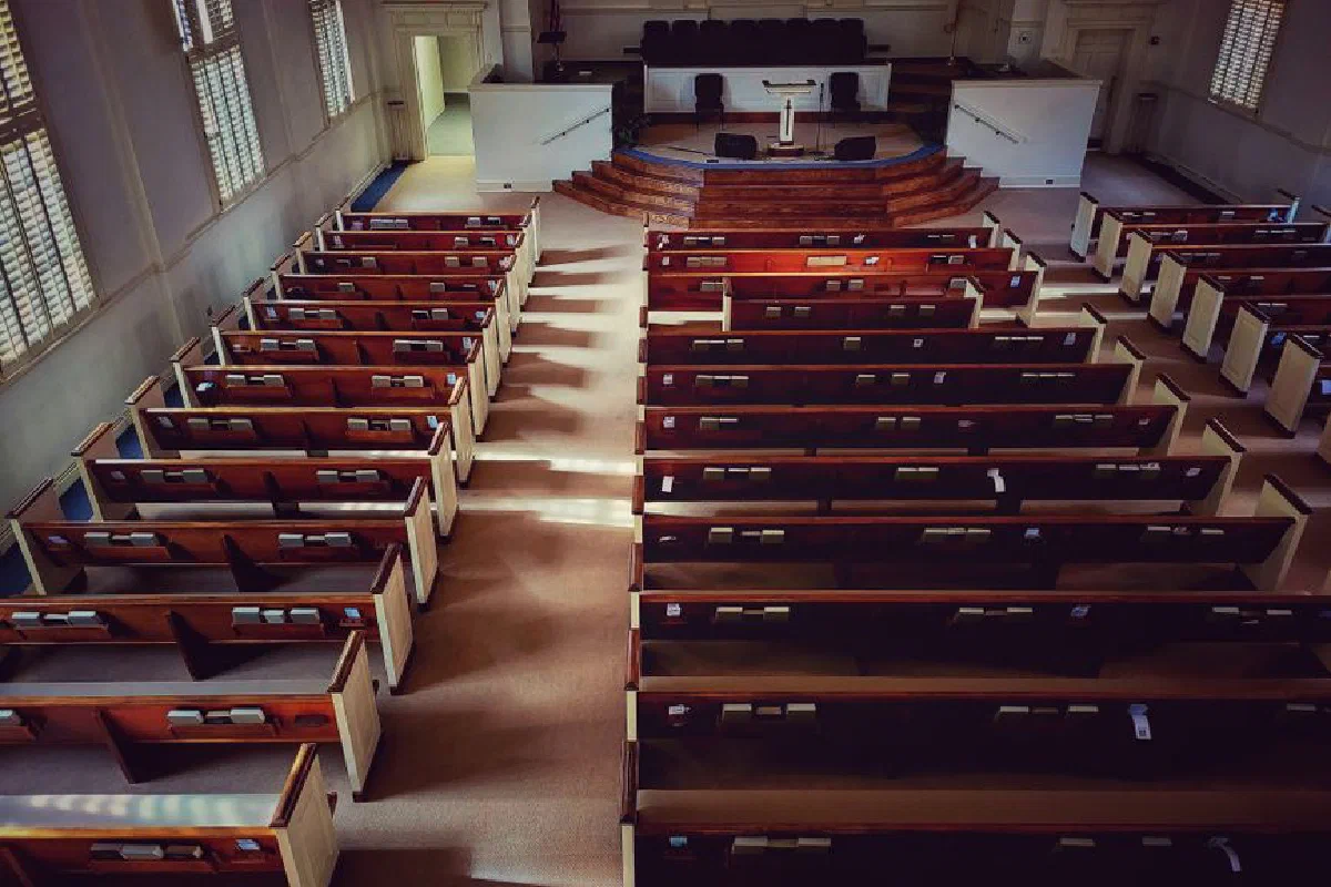 A serene, sunlit view of an empty church with neatly arranged wooden pews and an altar.