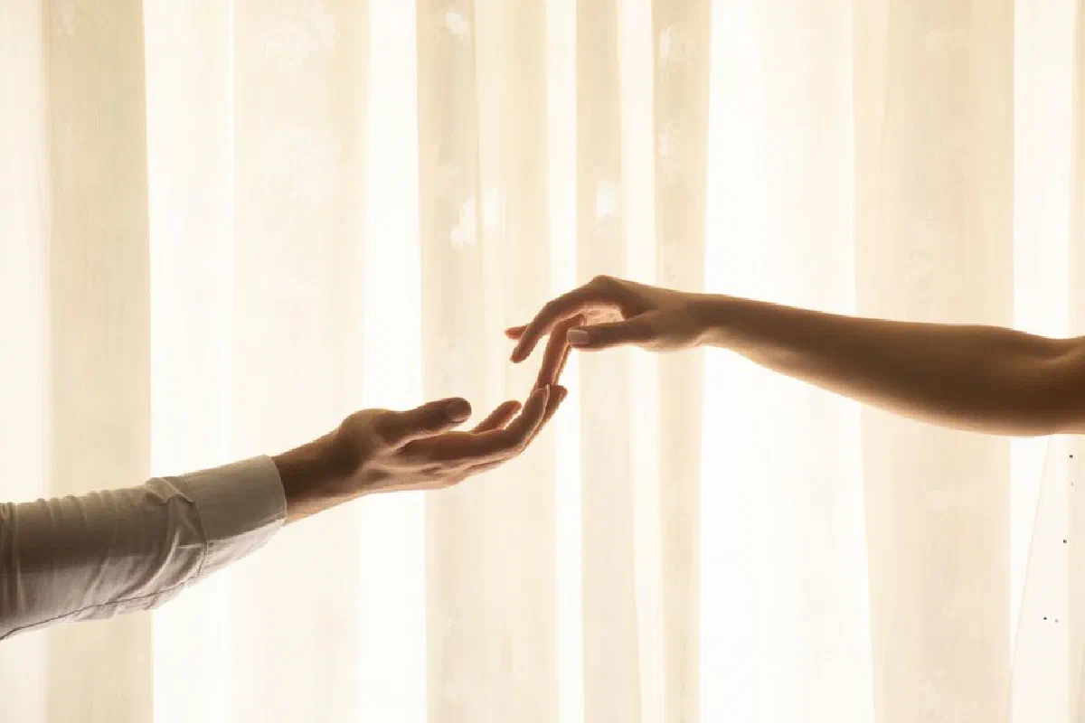 Two hands reaching out to each other in soft, warm lighting.