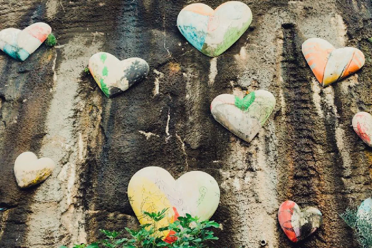 Heart-shaped stones with vibrant colors on a textured wall, symbolizing love and creativity.