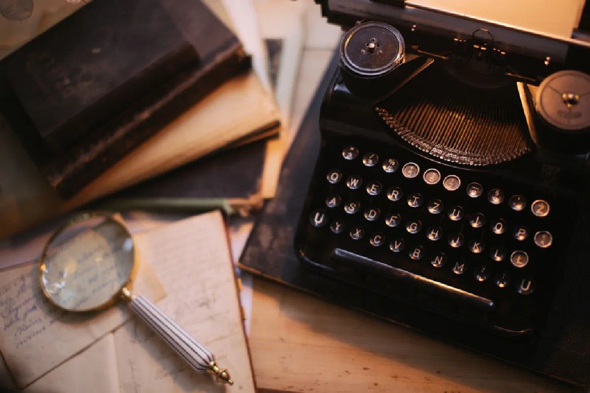 A vintage typewriter with a magnifying glass and old books on a desk, evoking nostalgia.