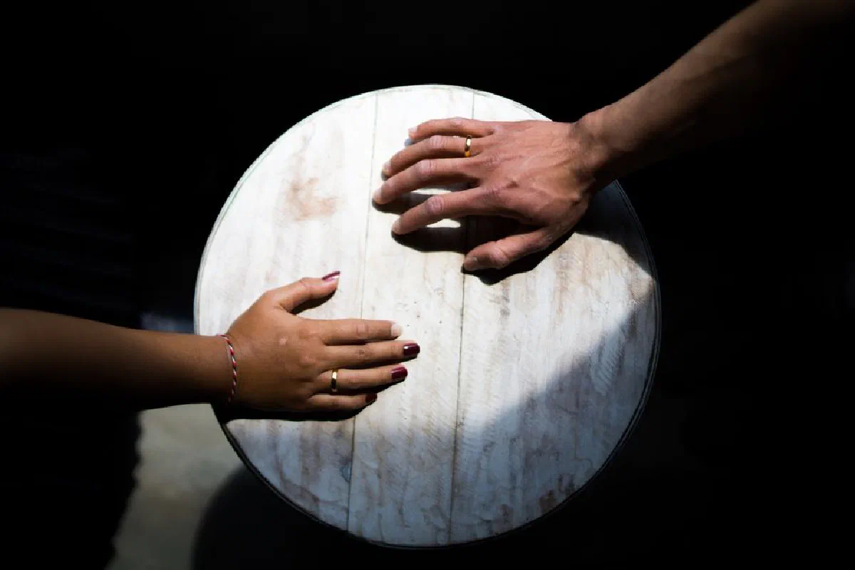 Close-up of hands adorned with rings on a wooden table, symbolizing unity.