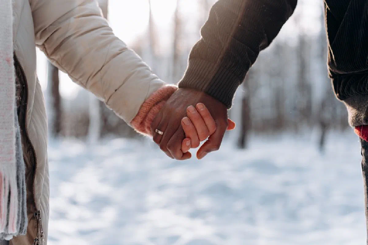 Close-up of a couple holding hands outdoors in a snowy winter setting, conveying love and togetherness.