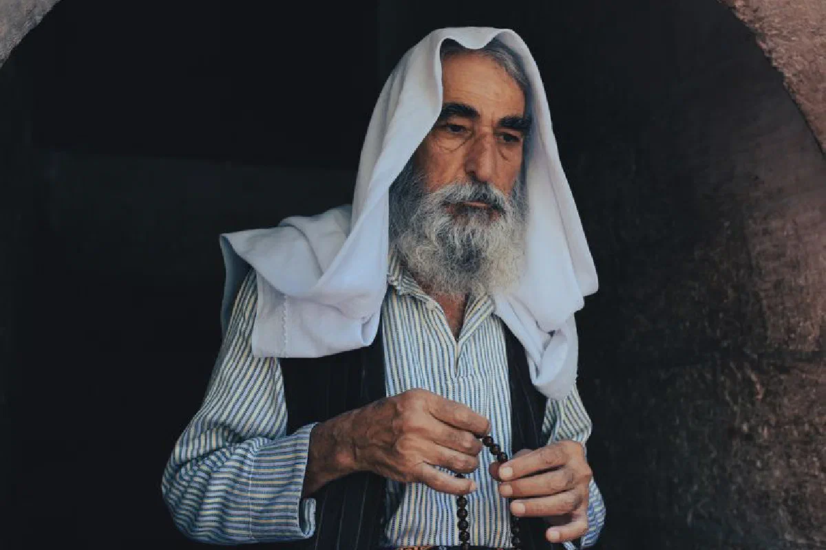 An elderly Middle Eastern man with a gray beard holding prayer beads, expressing faith and tradition.