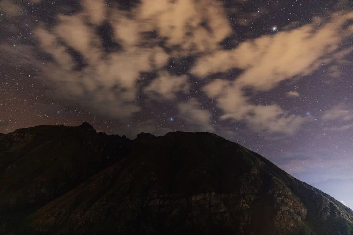 Starry night sky with clouds over a mountain landscape in Cusco, Peru.