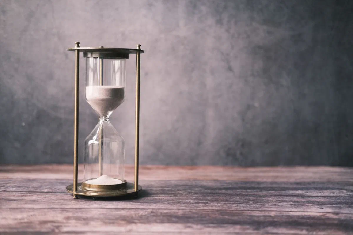 A classic hourglass with sand on a rustic wooden table against a soft gray background, offering ample copy space.