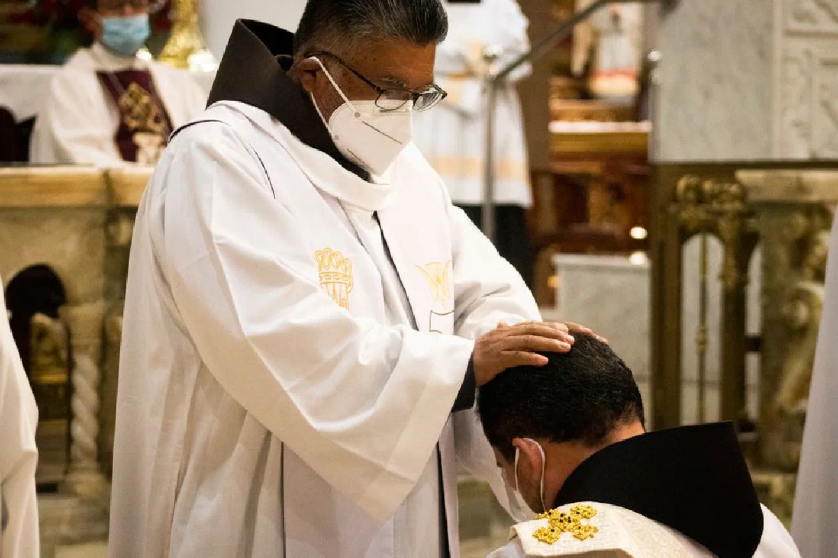 Priest giving a blessing during a religious ceremony in a church, both wearing face masks.
