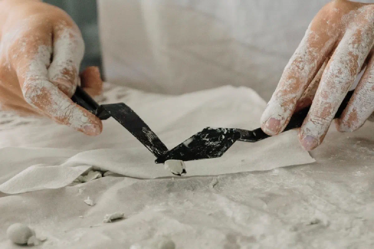 Artist shaping clay with scraper tools on a work surface. Perfect for DIY crafting and pottery themes.