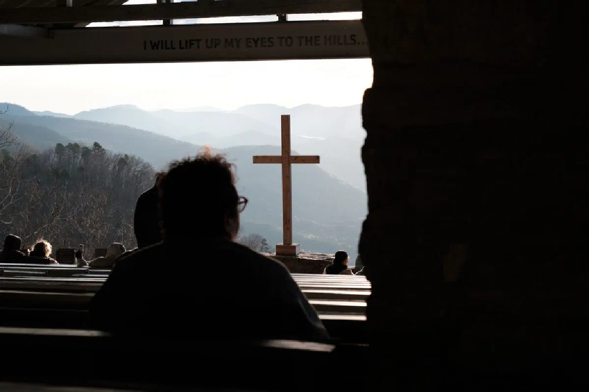 Serene church service outdoors with wooden cross and mountain landscape, evoking tranquility and spiritual reflection.