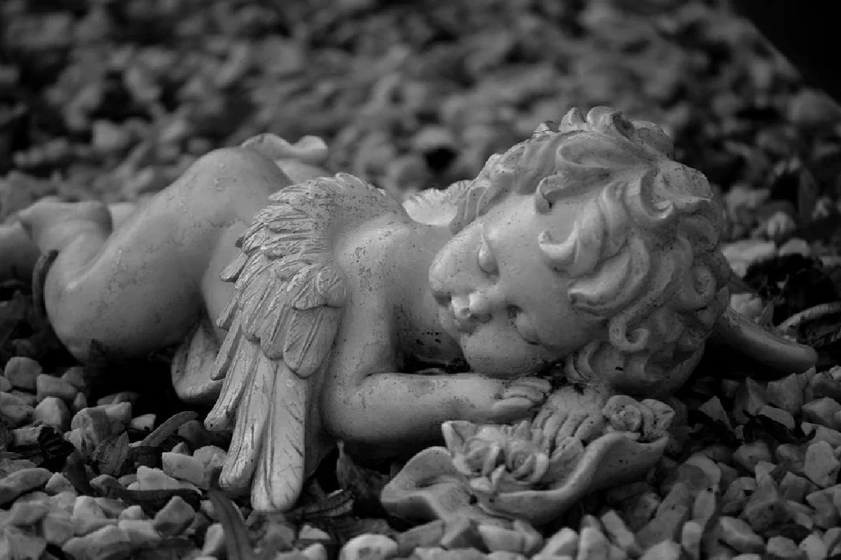 A grayscale photo of a sleeping angel statue on pebbles in Bocholt, Germany.