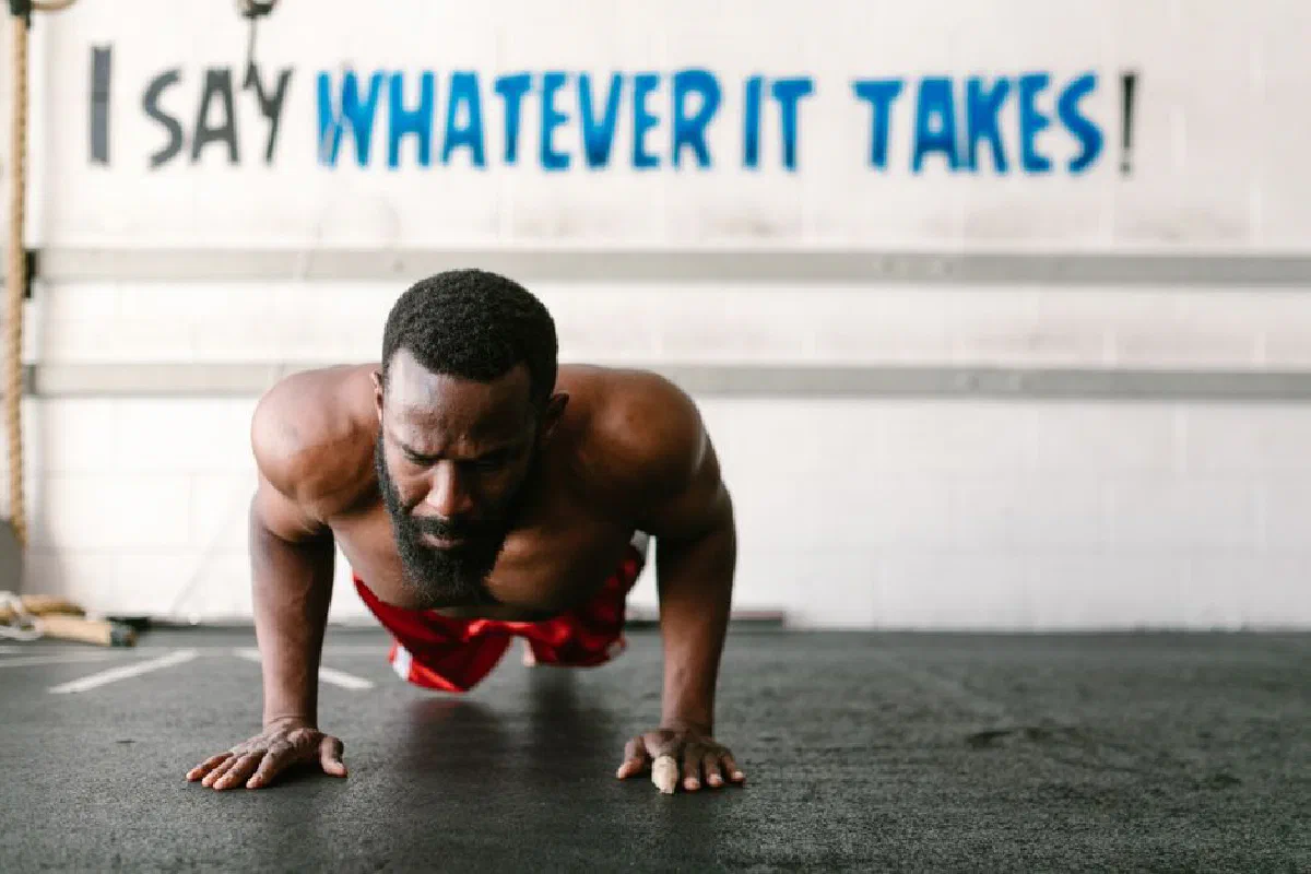 A man in a gym doing push-ups with a motivational quote on the wall behind him.