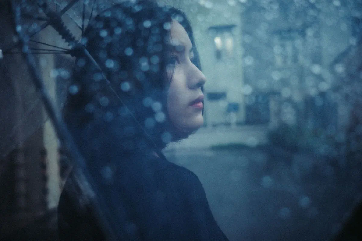 Artistic portrait of a woman holding an umbrella on a rainy day, with water drops and a moody atmosphere.