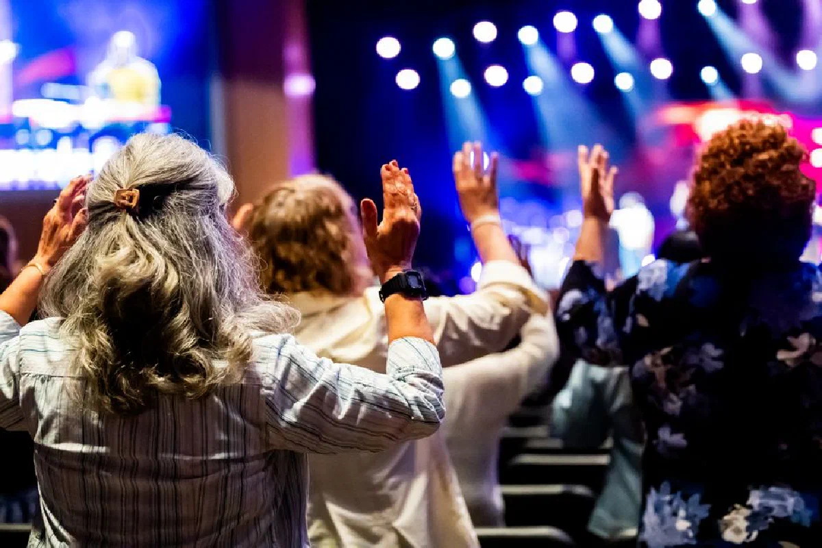 A group of people with raised hands attending a lively worship service inside a church.