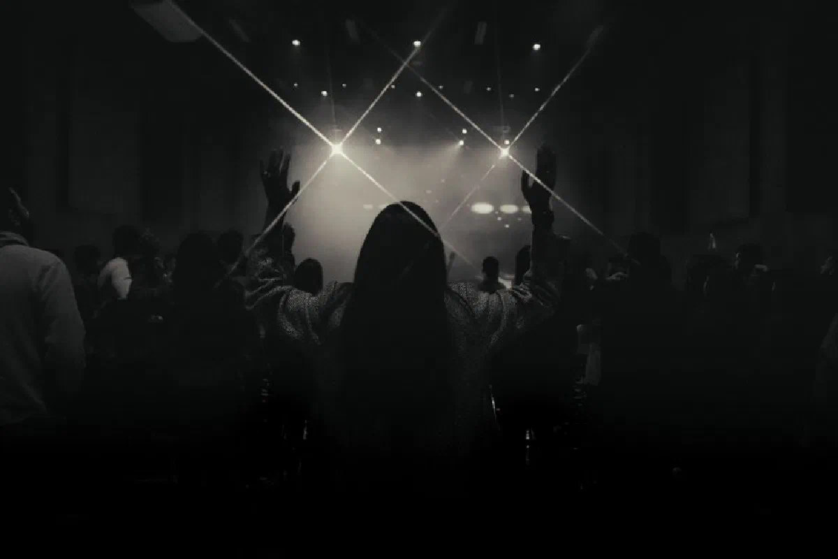 A black and white concert photo capturing a silhouetted audience in front of a bright stage.