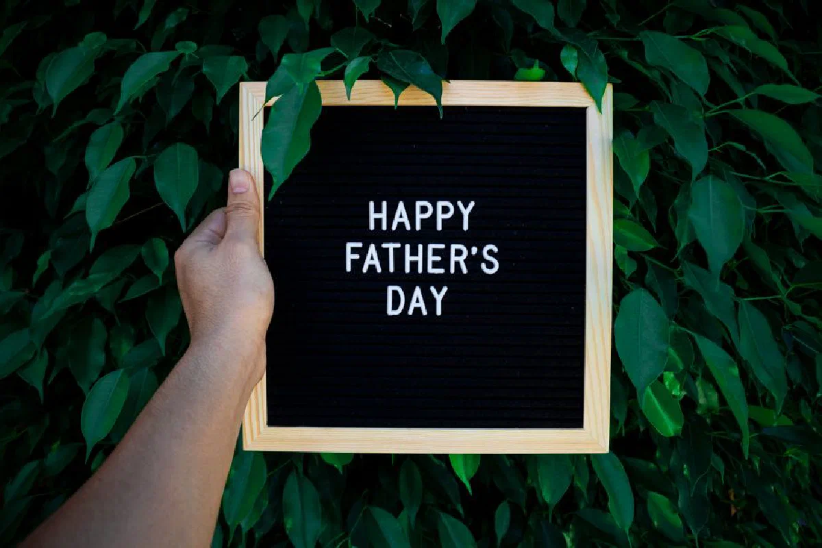 Wooden frame sign with 'Happy Father's Day' text held in front of vibrant green leaves.