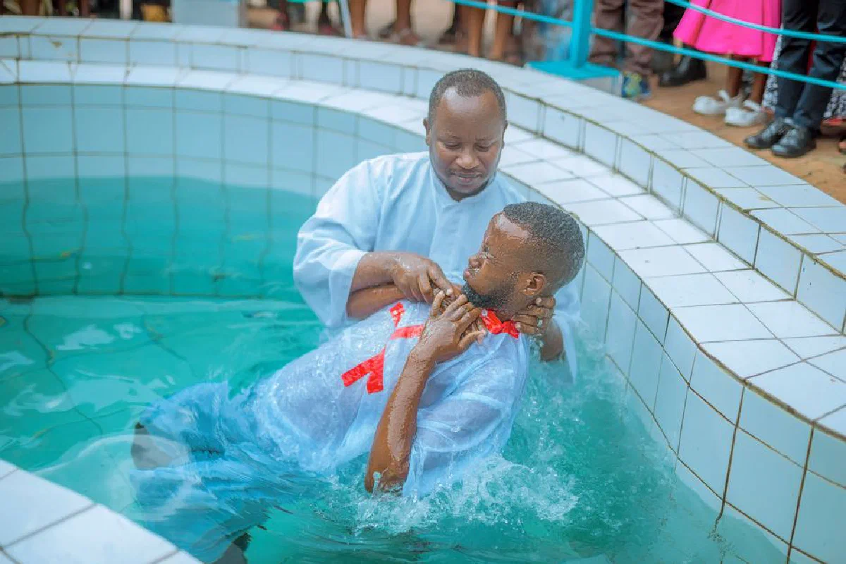 A baptism ceremony with a man being submerged in a pool by a religious leader.