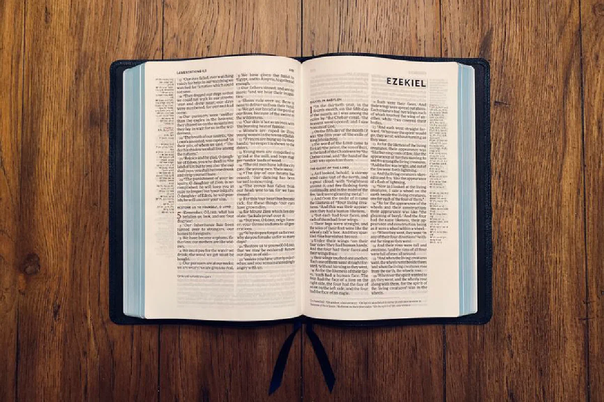 Open Bible displaying the Book of Ezekiel resting on a wooden surface.