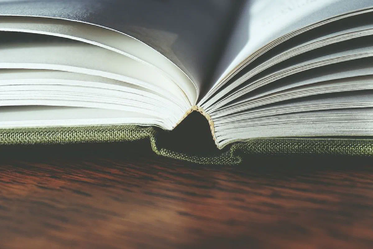 Detailed view of an open hardcover book on a wooden table, showcasing book pages and binding.