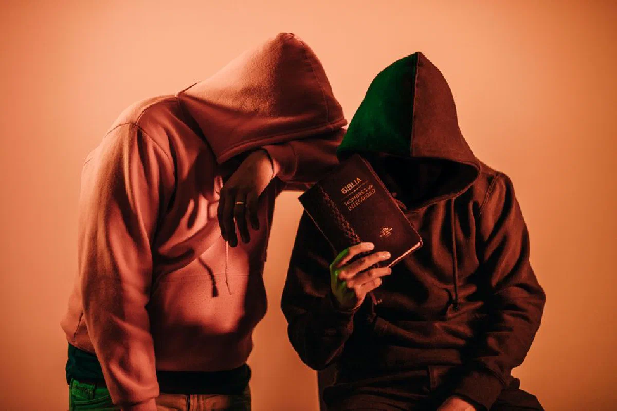 Two hooded figures holding a Bible, conveying mystery and faith.