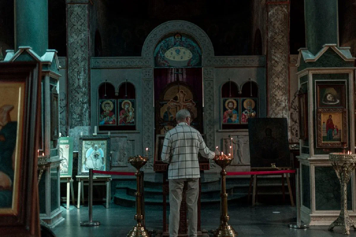 A man lights candles in a serene Georgian Orthodox church, surrounded by religious icons.
