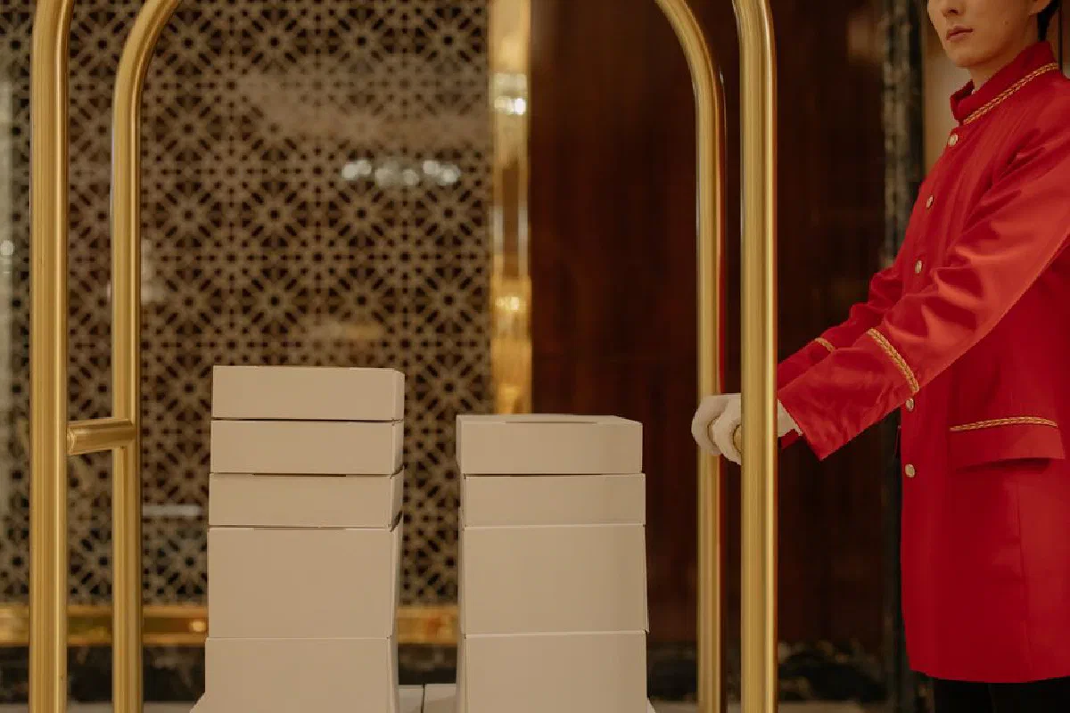 Hotel porter in red uniform assisting with luggage cart in a luxury hotel setting.