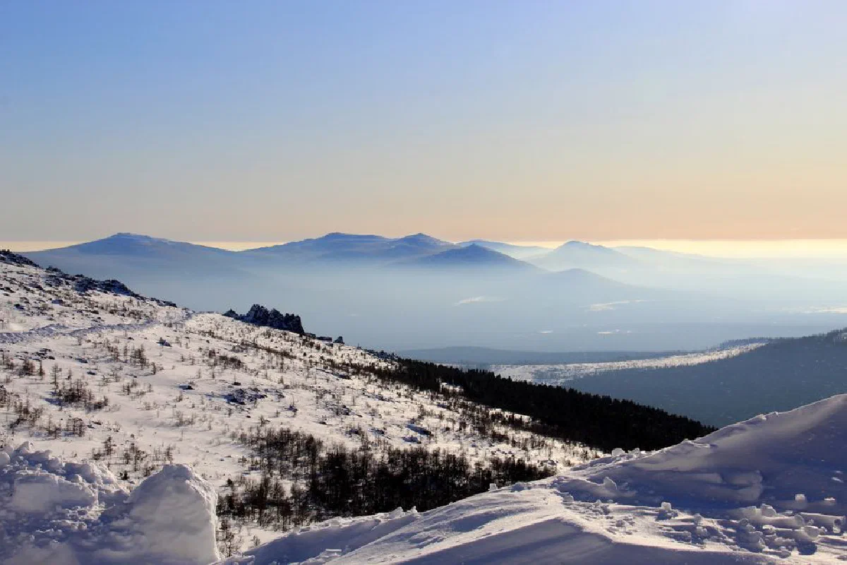 Breathtaking panoramic view of snow-covered hills and valleys during winter sunset.