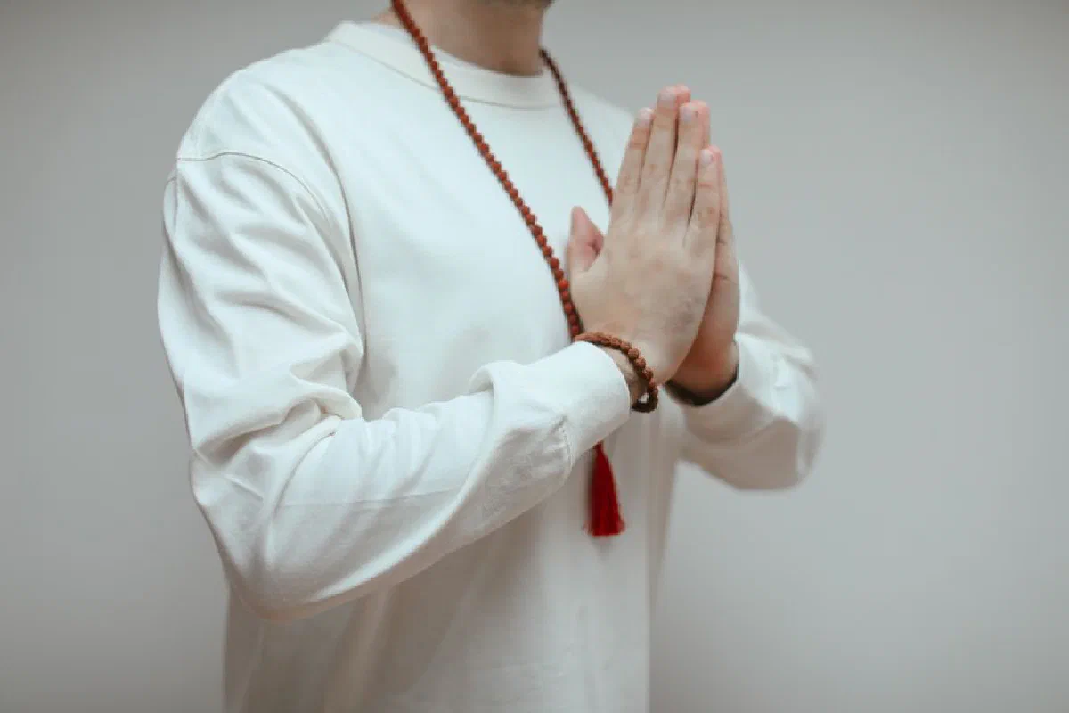 A person in white long sleeves meditating with prayer beads.