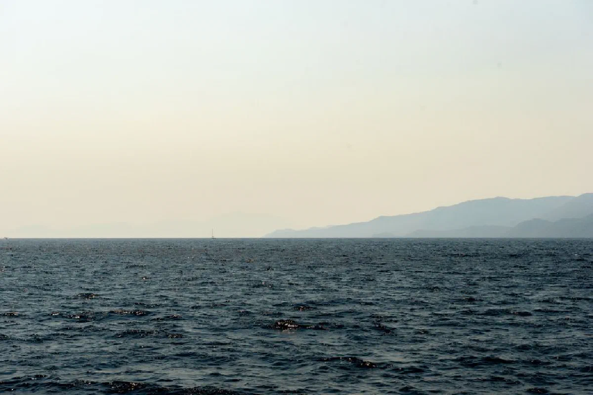 Peaceful ocean scene with distant mountain silhouette under a clear sky.