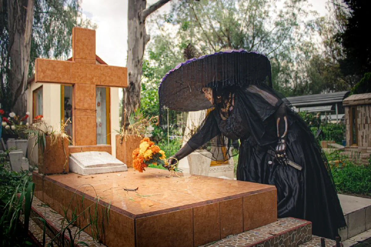 A person dressed in traditional Day of the Dead attire placing flowers on a grave in Mexico City.