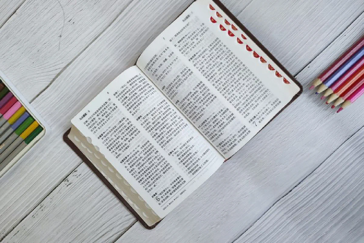 An open Bible with colored pencils on a wooden table, displaying religious text in Chinese.