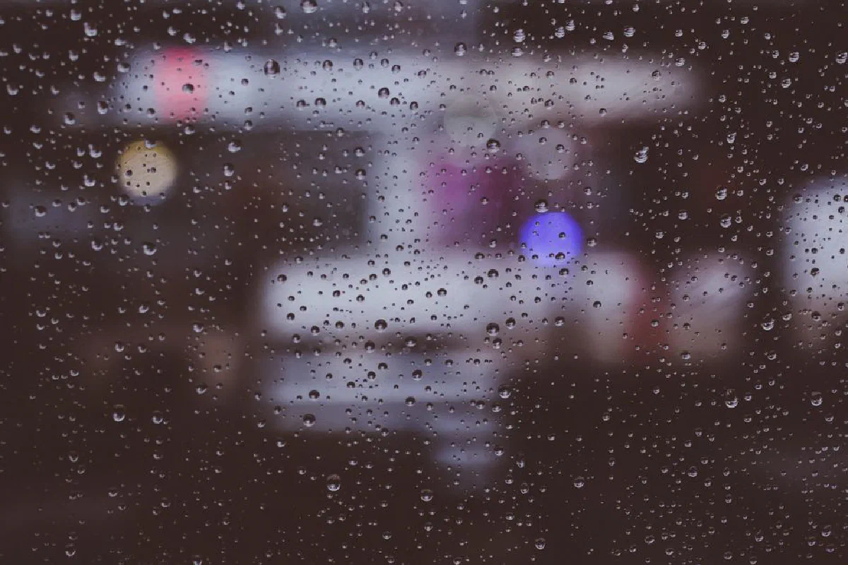 A moody, abstract view of raindrops on a window with a colorful bokeh background.