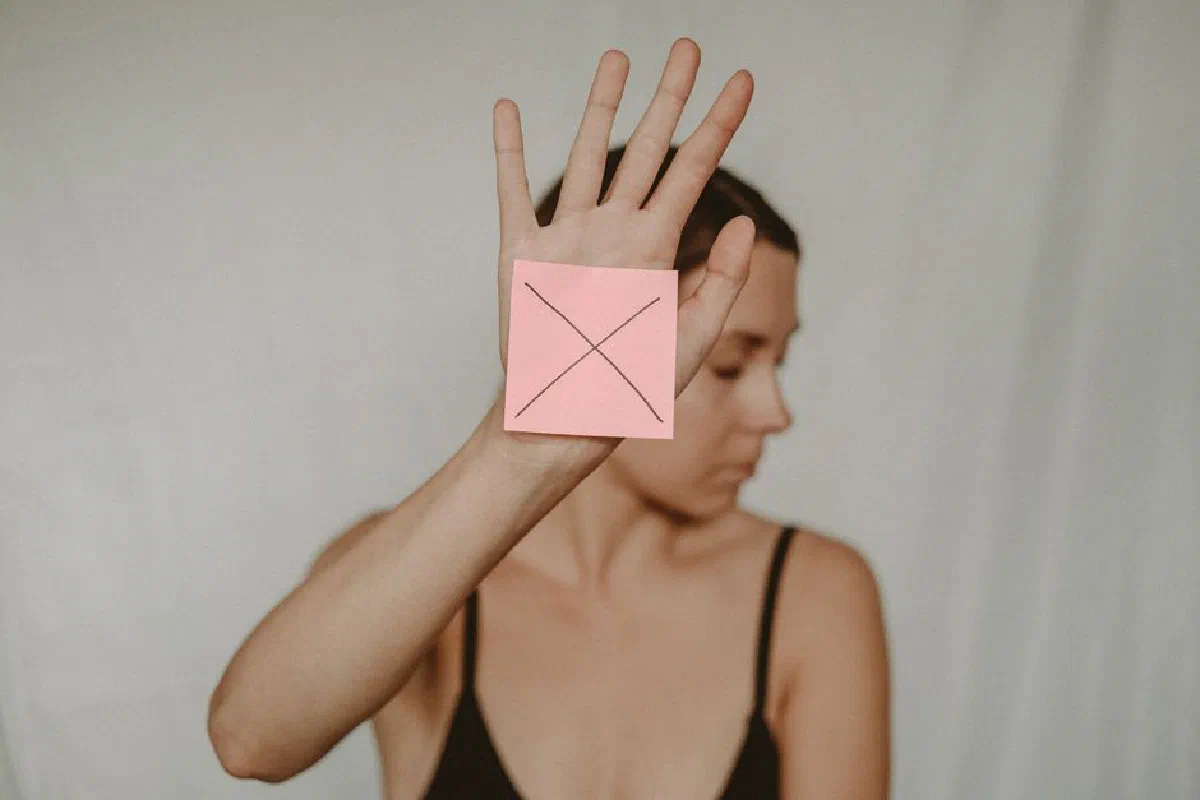 Young slender woman with closed eyes demonstrating sign stop with sticker on palm