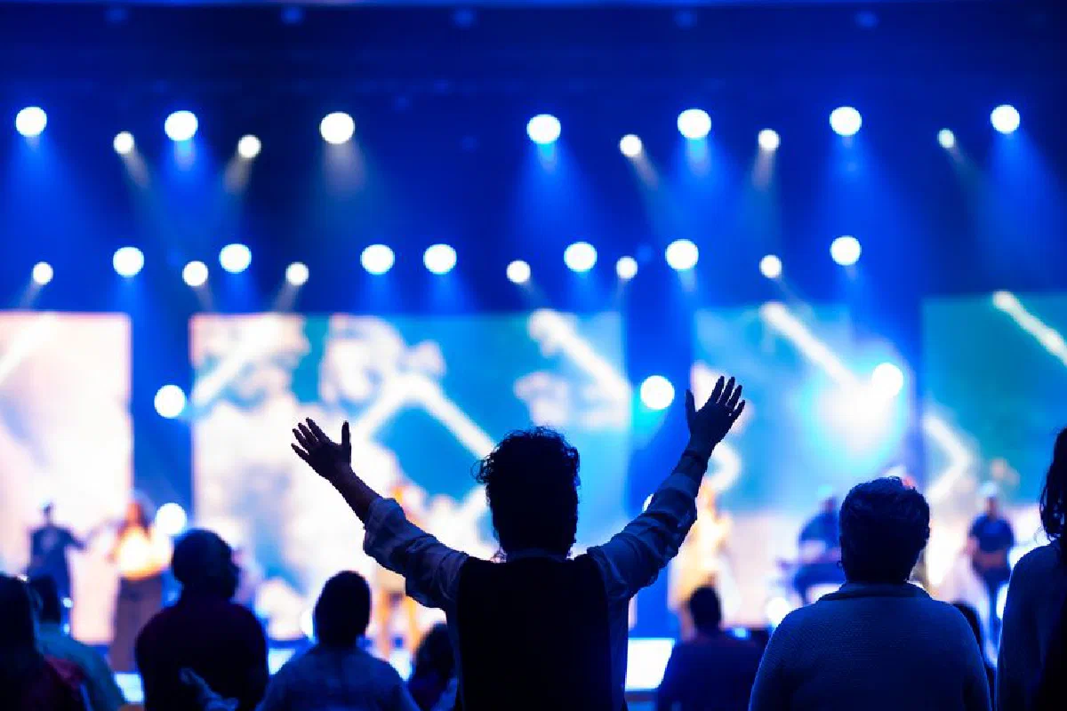 Audience enjoying a live concert with vibrant blue lighting and raised hands.