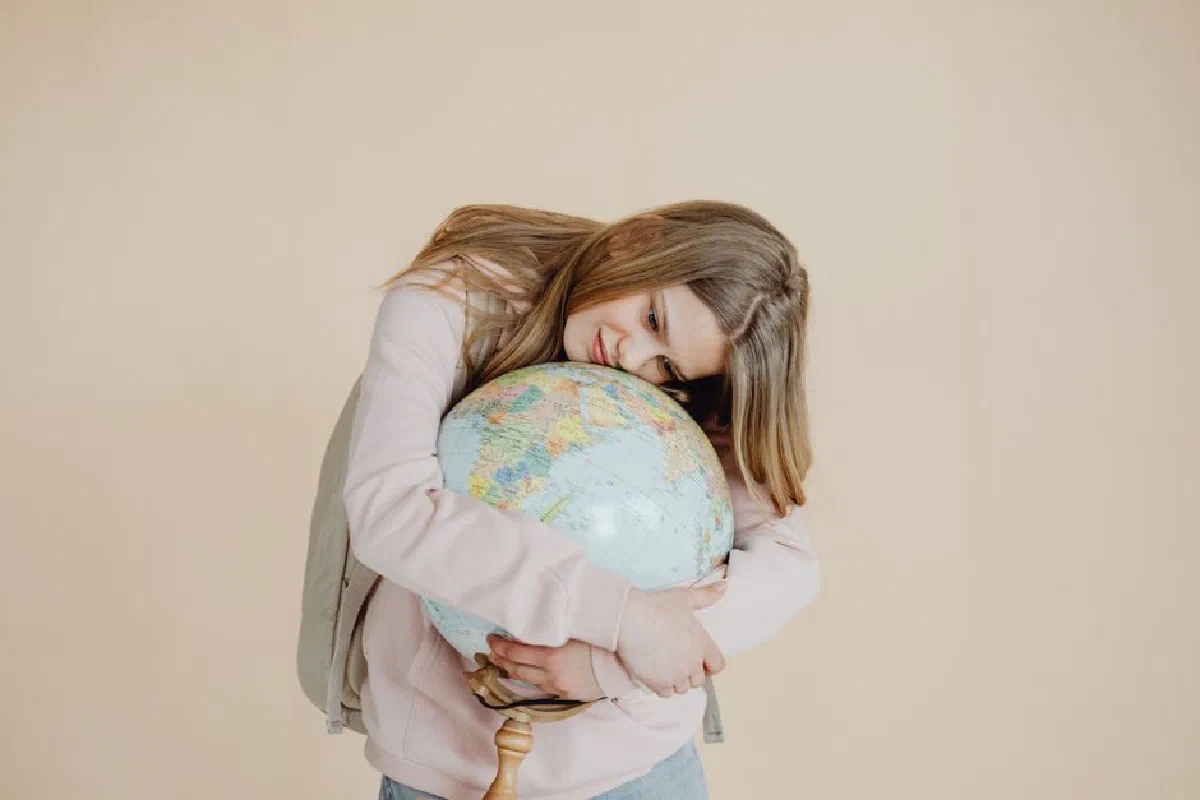 A young girl in a studio holding and hugging a globe, symbolizing global connection and love for Earth.