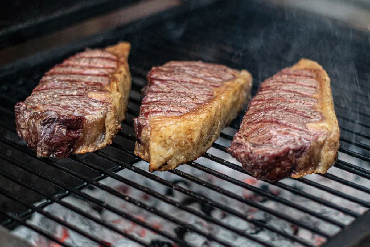 Close-up of three juicy steaks grilling on a barbecue, perfect for a summer cookout.