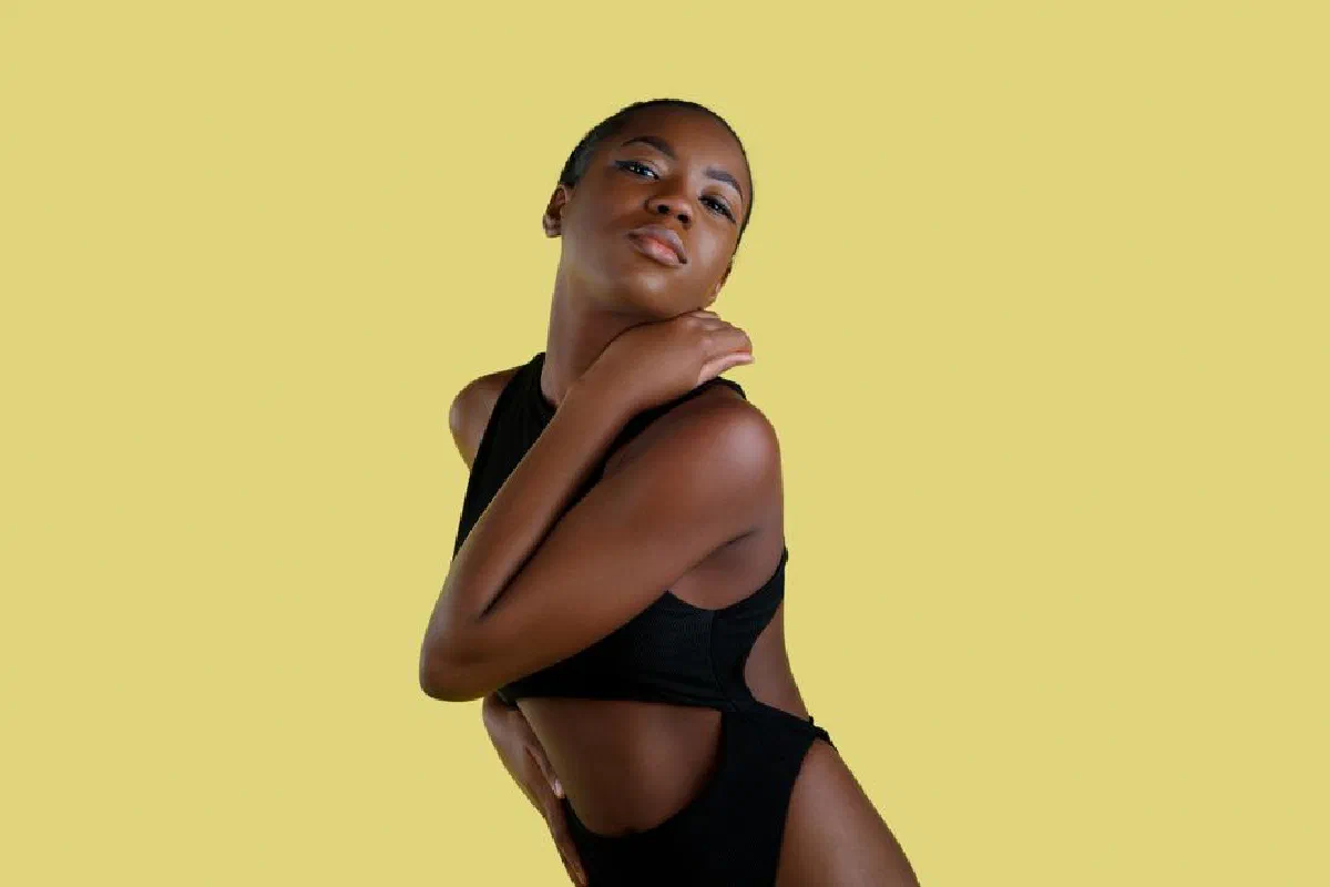 Graceful portrait of a woman in black swimwear posing against a vibrant yellow backdrop.