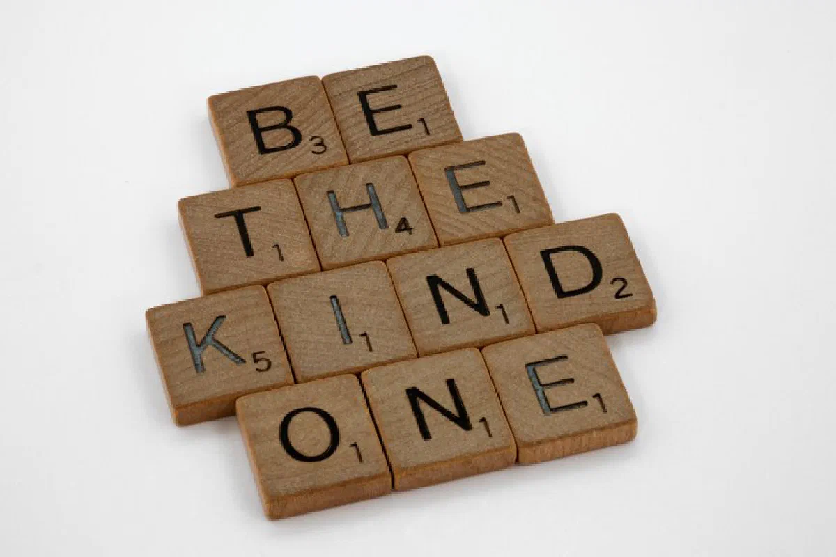 Close-up of wooden letter tiles forming the message 'Be the kind one' on a white surface.