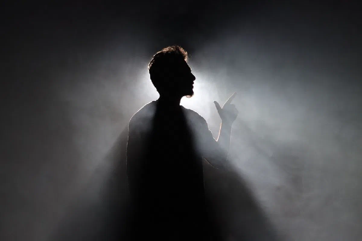 Backlit silhouette of a man pointing, surrounded by smoke in Bengaluru, India.