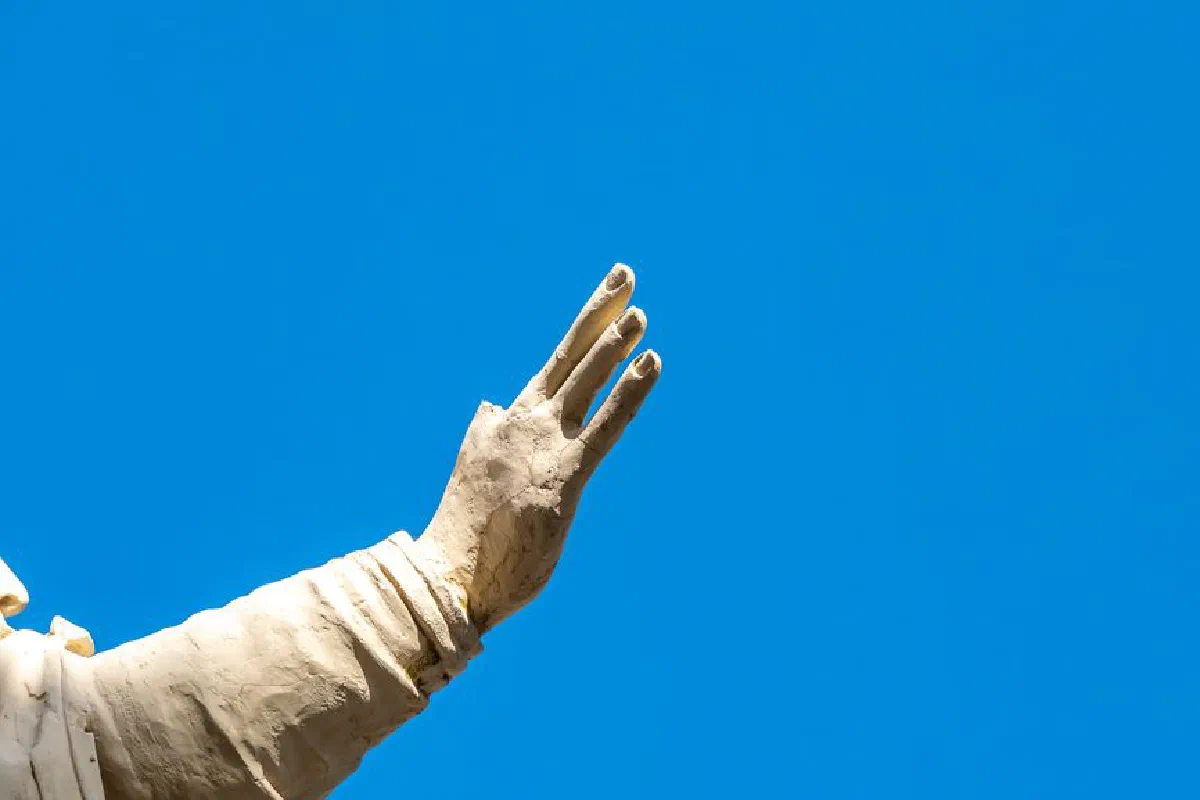 Close-up of a statue's hand gestures against a vivid blue sky, symbolizing expression.