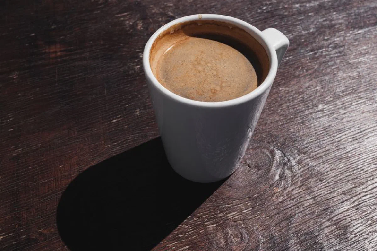 A freshly brewed cup of coffee on a rustic wooden table casting a warm morning shadow.